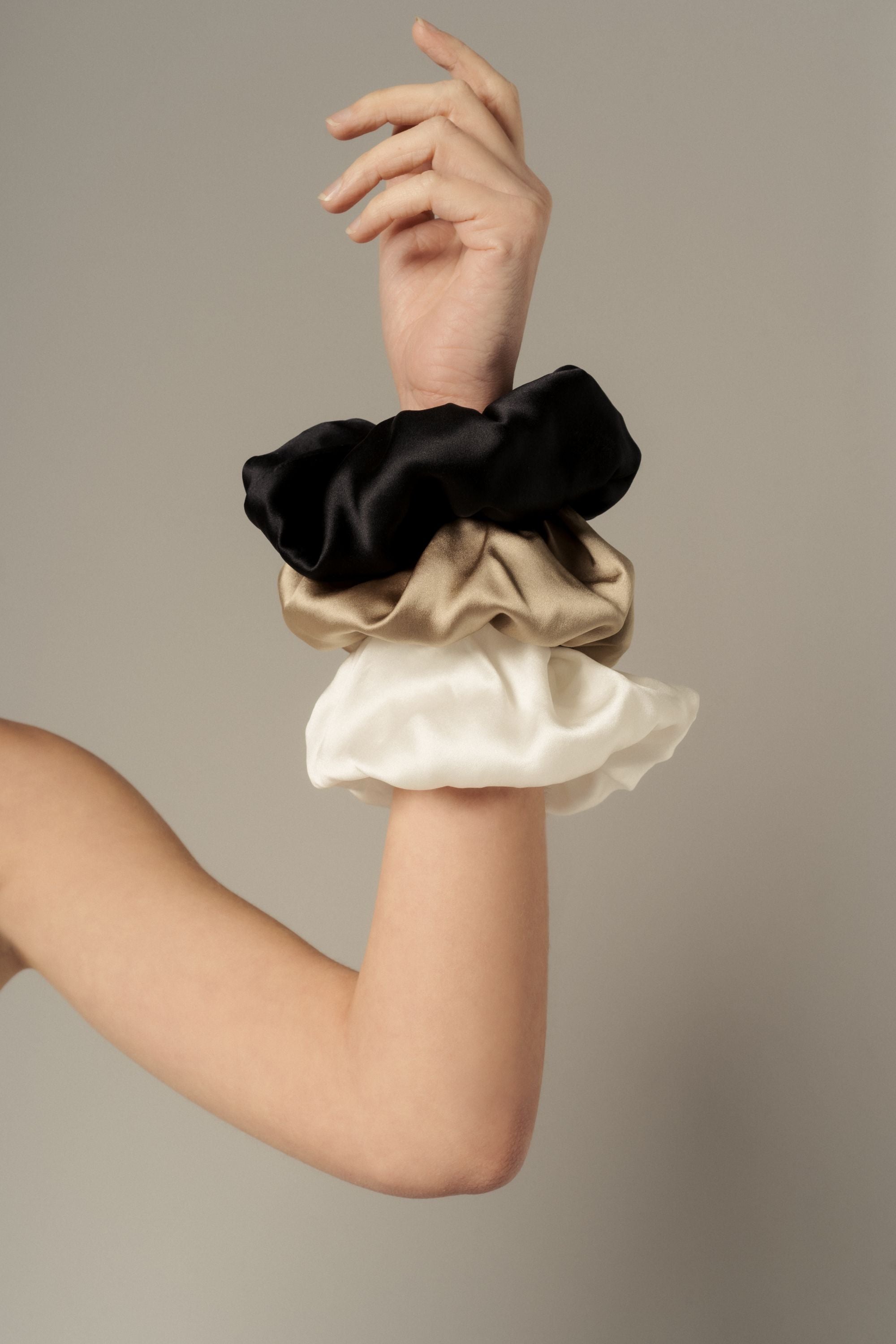 Organic silk scrunchies in black, gold sand and ivory, worn on the wrist, made in Italy