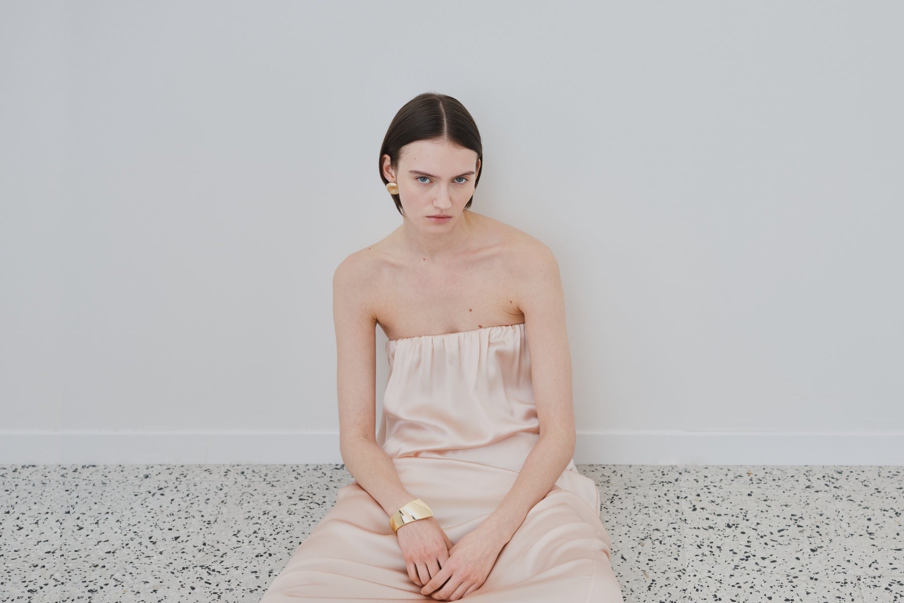 Model wearing a blush organic silk slip dress by HERTH in a minimal studio setting.