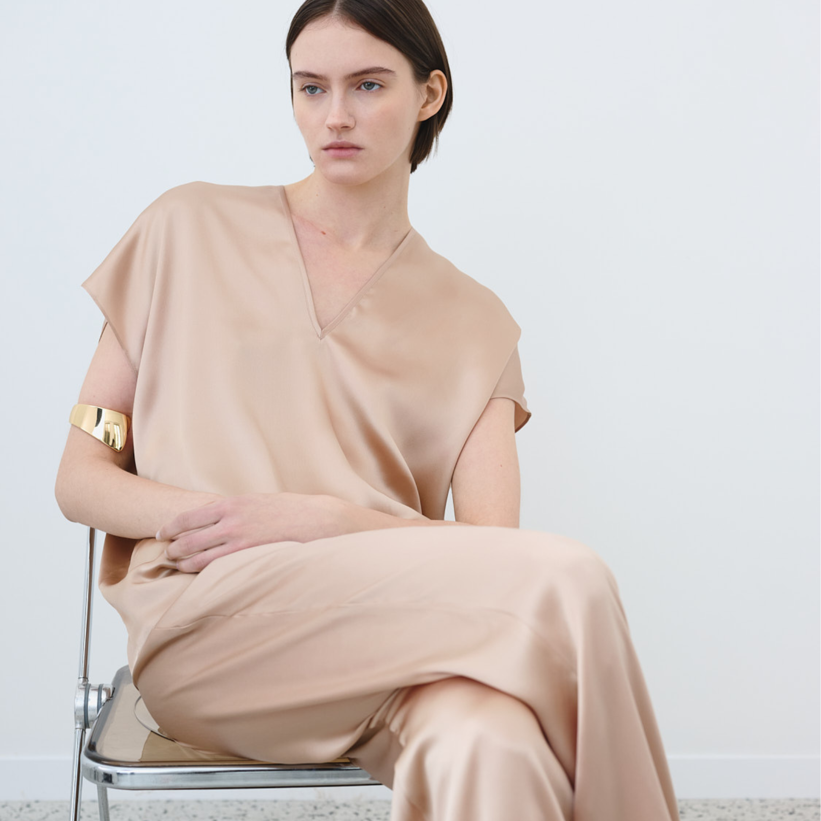 Woman wearing a coordinated organic silk top and trousers in beige, seated on a chair. Made in Italy.