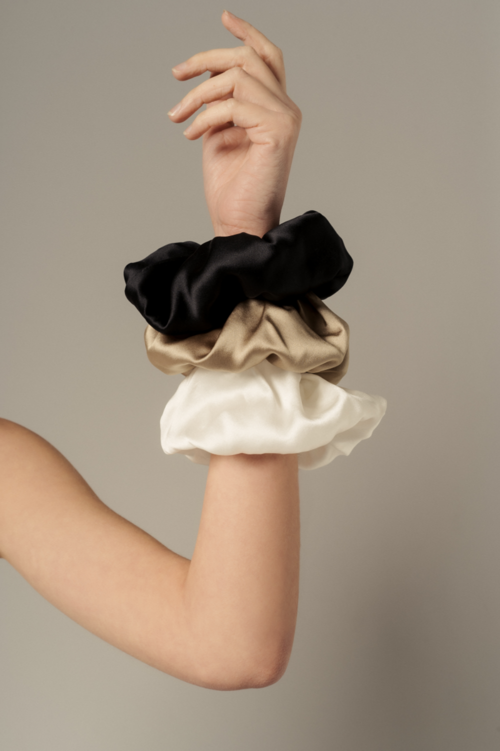 Editorial image of Edi scrunchies in black, gold sand, and ivory organic silk — worn on the wrist as elegant, sustainable accessories by HERTH.