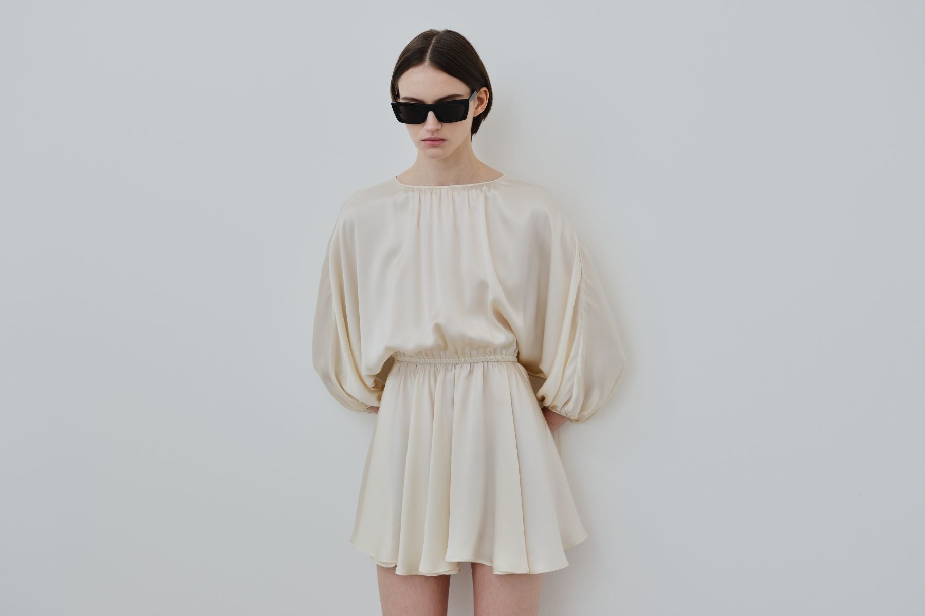 Model wearing the HERTH Ema dress in organic silk Almond, photographed against a minimal neutral backdrop