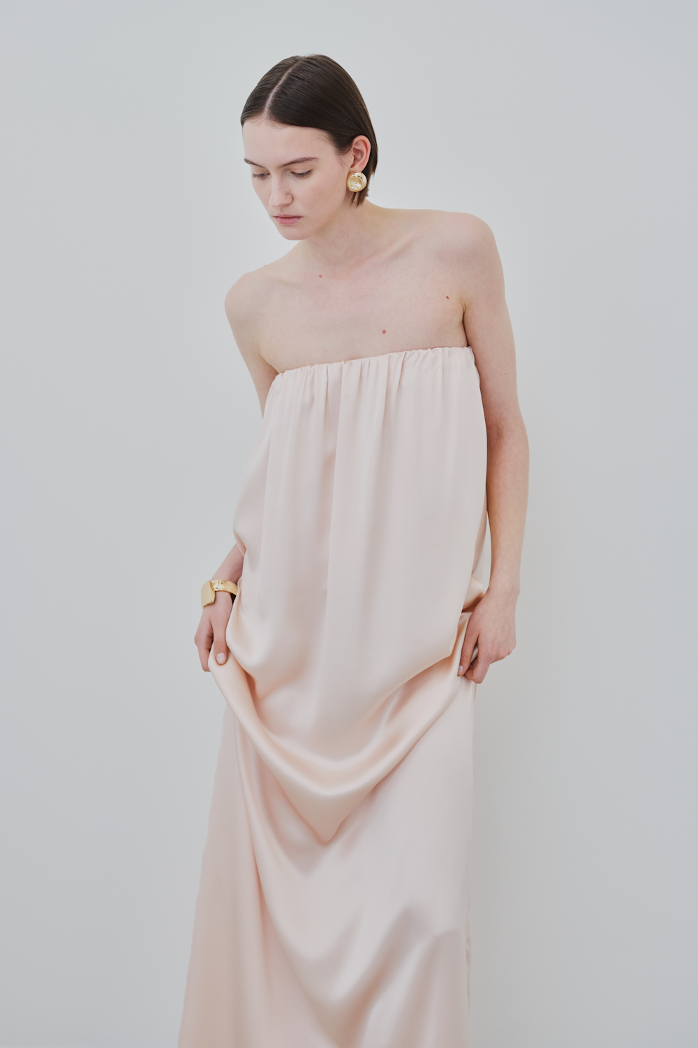 Model wearing the HERTH Erin dress in Whisper Pink — a strapless maxi dress crafted in organic silk with a fluid, sustainable silhouette. Luxury minimal womenswear by HERTH.