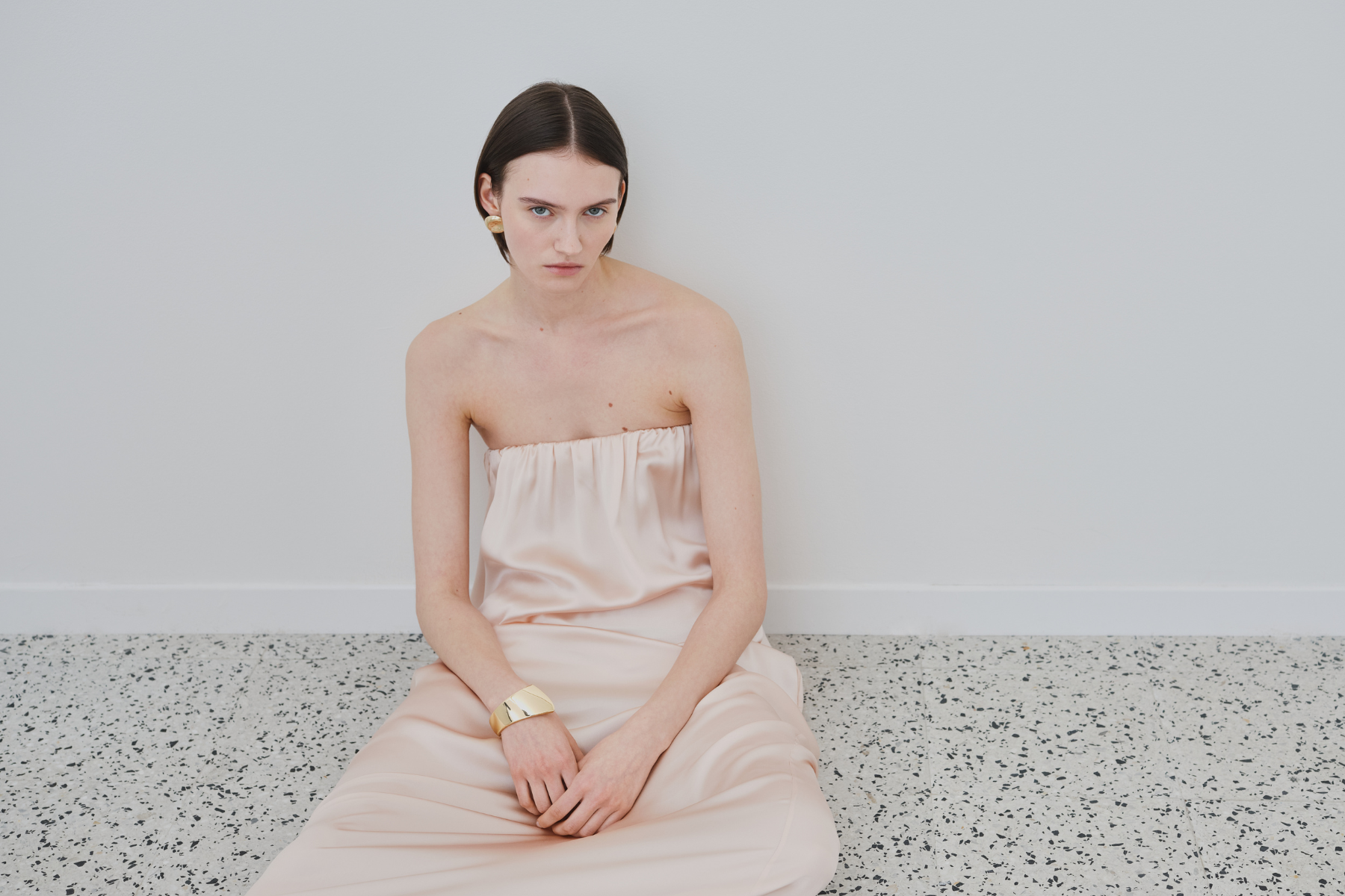 Model wearing a strapless organic silk dress in soft blush, photographed in a minimal setting for the HERTH Gift Guide.